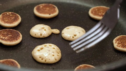 Process of cooking baked tiny pancake cereal - trendy quarantine food. Use fork to flip mini pancakes to other side on hot pan. Homemade breakfast. Slow motion.