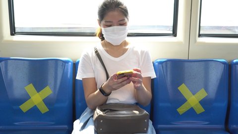 young asian woman wearing face mask sitting in the metro train and keep social distancing to prevent covid-19 or coronavirus infection. new normal lifestyle concept
