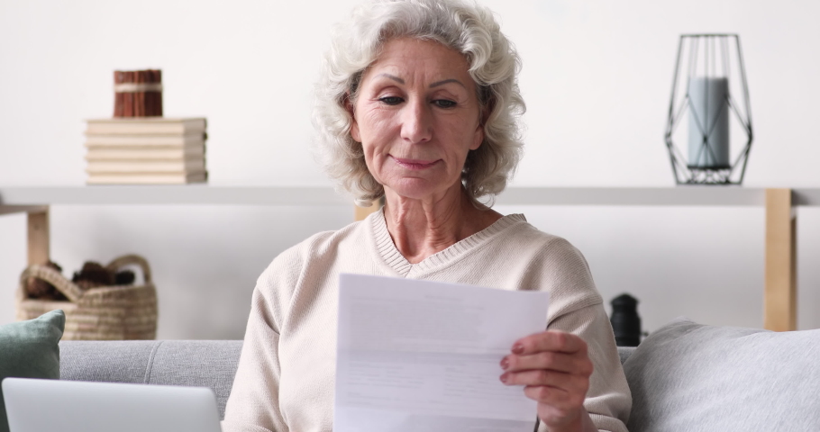 Head shot happy middle aged 70s retired woman holding paper letter, feeling excited by good news. Euphoric senior female client celebrating bank loan approve or last mortgage payment indoors. Royalty-Free Stock Footage #1053482405