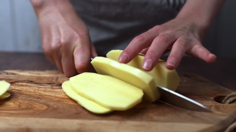 Cutting big potatoes in wedges for a French Fries meal. Slicing potatoes on a wooden cutting board. A woman's hand-chopping potatoes.
