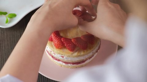 pastry chef decorating strawberry shortcake. woman hand putting strawberry on cake.