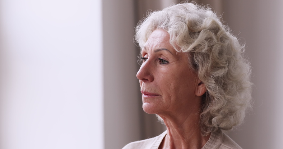 Head shot unhappy sad old mature woman looking at window, feeling loneliness indoors. Depressed unhappy middle aged 60s grandmother suffering from mental disorder, thinking of bad health diagnosis. Royalty-Free Stock Footage #1053491297