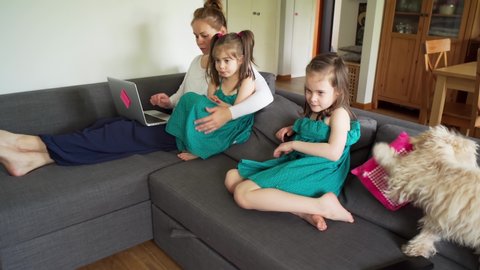two little sisters watch tv and mother works remotely on a computer during a pandemic