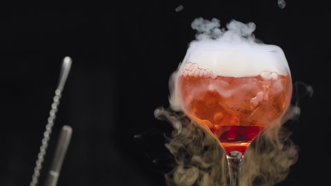 Close up glass of red cocktail with dry ice slowly rotating and moving on a slider. The glass is wrapped in steam. Bar drinks and cocktails