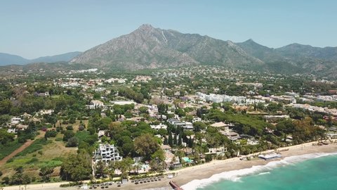Sensational aerial view of luxury and exclusive area of Marbella, golden mile beach, view of Puente Romano Bridge and in Background famous La Concha mountain. Emerald water color Drone going backwards