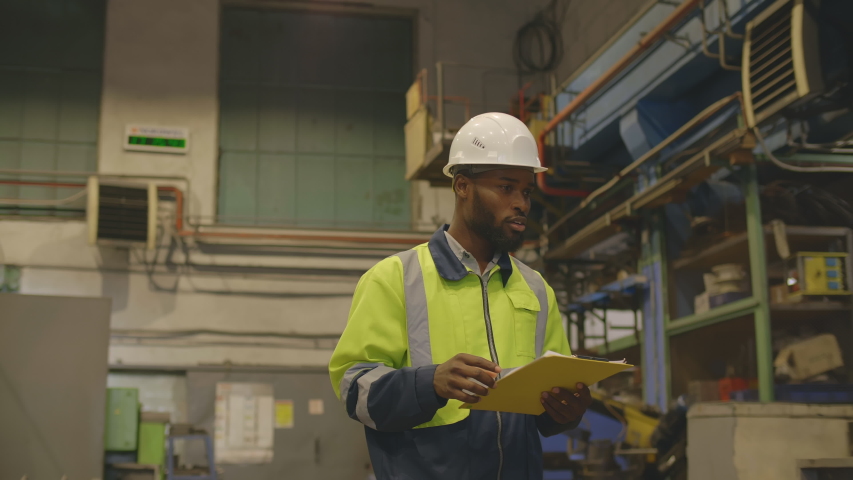 Portrait of afro-american supervisor writing down report in clipboard during inspection of manufacturing plant at industrial factory. African engineer doing inventory | Shutterstock HD Video #1053499361
