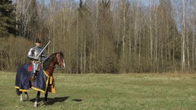 Video 4k footage, A young adult man in knightly armor rides across the field on a horse in armor