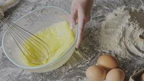 Girl's hand whip natural organic eggs in a glass bowl on a background with flour and eggs. Slow motion, Full HD video, 240fps, 1080p. Step by step preparing of homemade bake.