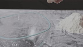 Fresh organic egg falling into bowl. Hand is breaking egg in a glass bowl on a flour background. Preparing ingredients for homemade baking. Slow motion, Full HD video, 240fps, 1080p.