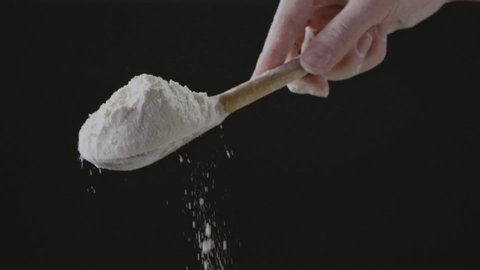 Slowly pouring flour from wooden spoon in a female chef hand on a black background. Slow motion, Full HD video, 240fps, 1080p. Step by step homemade dough preparation.