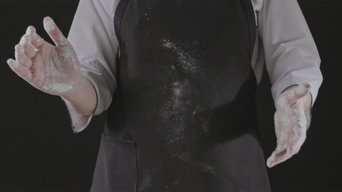 Girl chef is clapping his hands filled with white flour on a black background. Slow motion, Full HD video, 240fps, 1080p. Process preparing of homemade pastry.