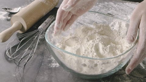 Hands of professional baker take flour from glass bowl and put on a wooden rustic background. Rolling pin and whisk on a table. Slow motion, Full HD video, 240fps, 1080p. Process preparing of pastry.