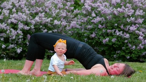 Children's Day. Young mother does body workout with her baby in a city park. Relaxation of the psyche of mother and child. Healthy lifestyle. Harmonious parenting by conscious parents. Family school. 