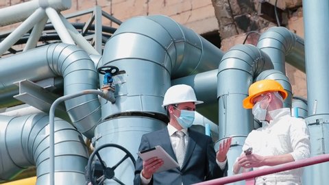 Manager and worker in protective masks face. Organization work in industrial sector during quarantine. Conflict of manager and worker on gas and oil production platform. Factory technical pipes.