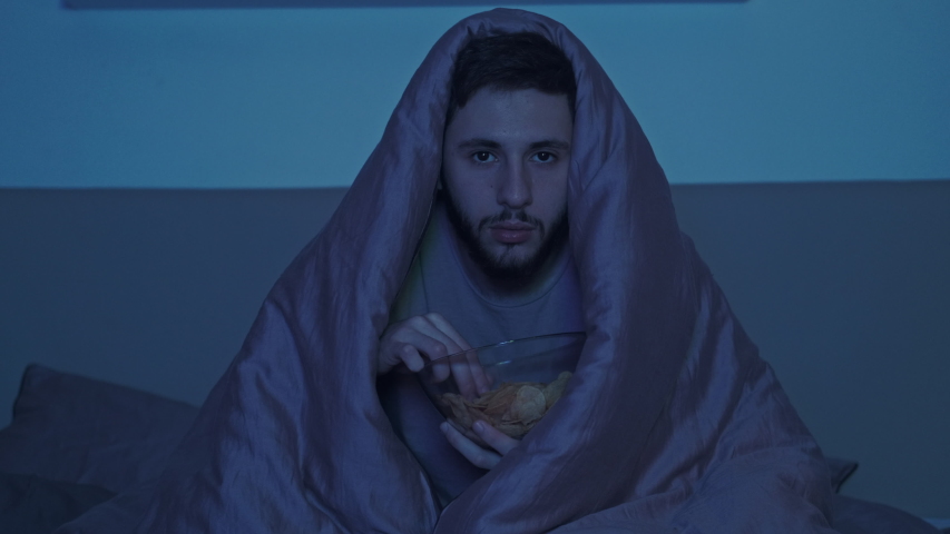 Late home leisure. Sleepless night. Scared man in blanket watching horror movie in dark bedroom. Royalty-Free Stock Footage #1053505481