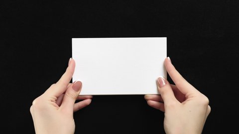 Advertising card mockup. Female hands holding white blank paper with copyspace on black background.