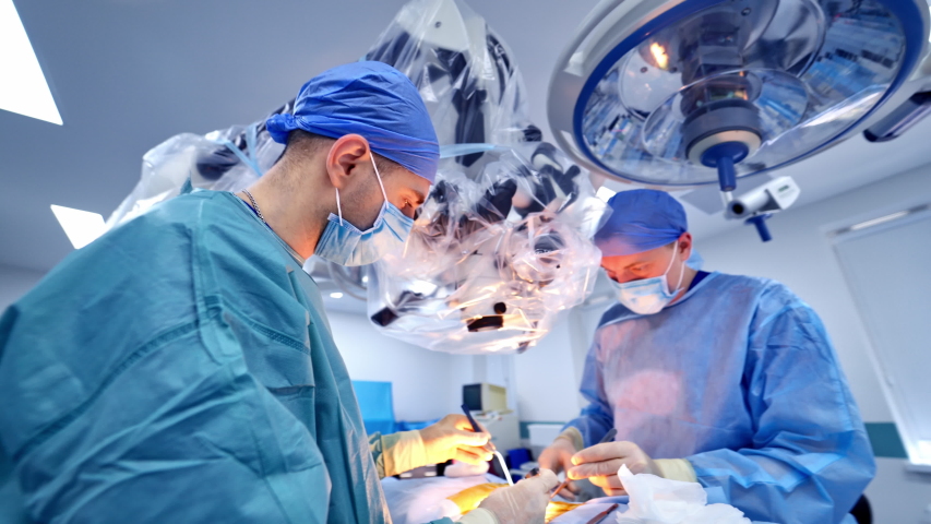 Surgeons working in operating room.. Surgeons working in operating room. Hospital background. Two male doctors at work. Circular background of an operation on a spinal cord, vertebra. Royalty-Free Stock Footage #1053506120