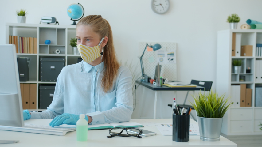 Woman in face mask and gloves is working with computer then waving good-bye to colleague in office. Pandemic healthcare and workplace concept. | Shutterstock HD Video #1053509147