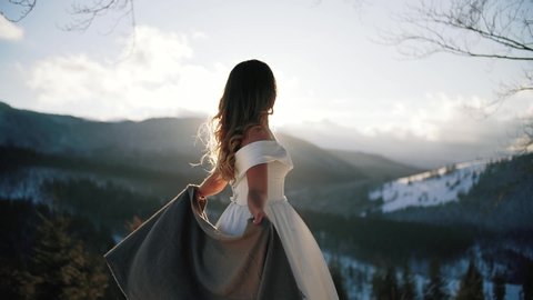 Newlyweds. Lovely young The bride in a white dress, covered with a large scarf, on top of the mountain, Winter, mountains Wedding couple. Happy family. Slow motion.