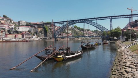 Porto / Portugal - May 16, 2020: AERIAL DRONE FOOTAGE - The iconic Rabelo Boats, the traditional Port Wine transports, with the Ribeira District and the Dom Luis I Bridge over the Douro River, Porto.