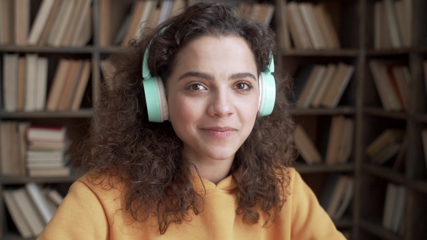 Happy positive latin teenage girl laughing at funny joke looking at camera in library. Cheerful hispanic teen school college student wear headphones having fun, smiling ethnic face close up portrait. Royalty-Free Stock Footage #1053511181