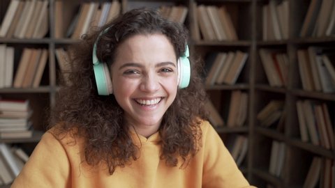 Happy positive latin teenage girl laughing at funny joke looking at camera in library. Cheerful hispanic teen school college student wear headphones having fun, smiling ethnic face close up portrait.