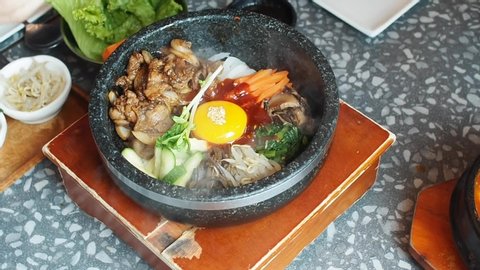 Popular Korean food on the table;  bibimbap or mixed rice with vegetable, pork and raw egg yolk served in hot stone pot. Selective focus.