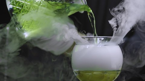 Making Grape Martini Cocktail. Close up bartenders hands pouring water into a glass with dry ice, putting cocktail glass there and pouring green martini in it. The glass is wrapped in steam