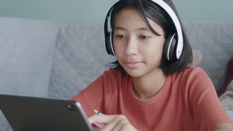 Asian girl is study online via the internet on tablet with headphone while sitting at home morning, Asia Children find information studying on Digital tablet. Concept of online learning at home