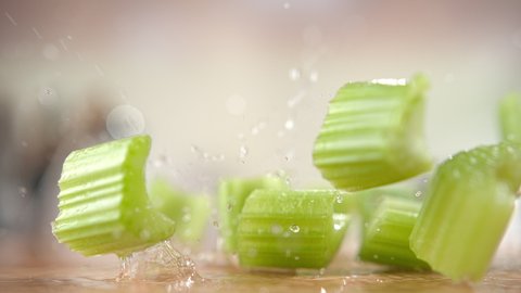 Raw Chopped Celery Falling onto the Wooden Cutting Board Bouncing and Splashing Water Drops around the Kitchen