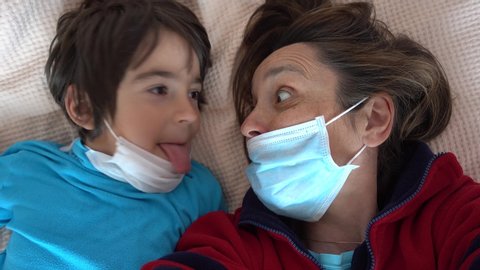 4K Covid-19 isolation selfies - Comic mother and child in masks grimace and make faces on camera
