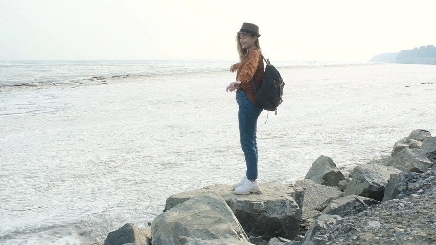 traveler stands on stone cliff by sea enjoys vacation raises hands up is happy.