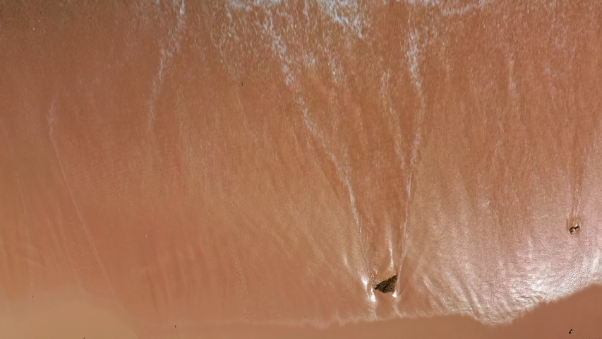 Aerial top view of ocean blue waves break on a beach. Sea waves and beautiful sand beach aerial view drone shot. Bird's eye view of ocean waves crashing against an empty sand beach from above. | Shutterstock HD Video #1053525074