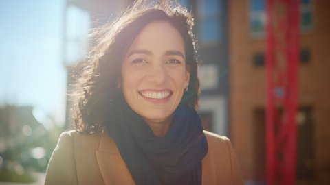 Portrait of a Gorgeous Dark Haired Hispanic Woman Smiling Charmingly while Standing in the Middle of Modern Urban City Landscape, Wearing Spring Coat. Happy Young Woman Enjoys Life