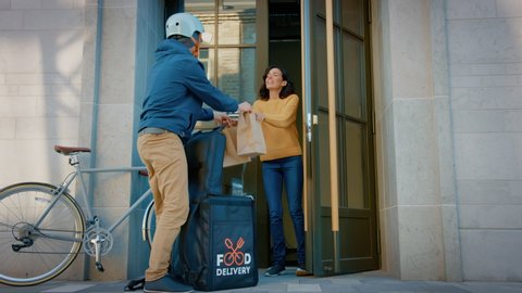 Happy Food Delivery Man Wearing Thermal Backpack on a Bike Delivers Restaurant Order to a Beautiful Female Customer. Courier Delivers Takeaway Lunch to Gorgeous Girl in Urban Office Building.Side View
