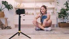 Teen vlogger. Online coaching. Enthusiastic girl using smartphone camera on tripod to record speech.