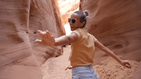 SLOW MOTION: Young adventurous couple holding hands woman leading boyfriend running into narrow canyon in the desert POV travel concept. Female waving hand.