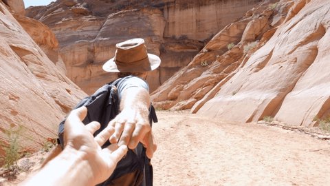 SLOW MOTION: Adventurous couple hiking in the desert, man holding partner's hand leading the way towards magical rock formation canyon