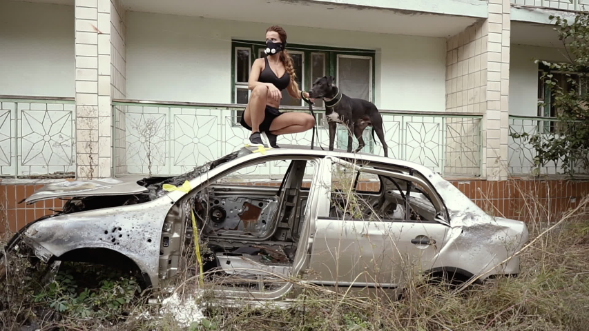 Post apocalypse. A girl is standing in a car and holding a dog on a leash.
