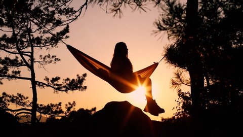 Awesome shot of beautiful young european woman seated in a hammock working with a laptop on a sunset background. Girl sitting in hammock, relaxing on top of mountain