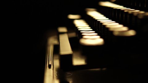 A man or woman works on a typewriter. Old typewriter on a dark background, close-up shot. Fingers press keys in dimly lit desk lamps. A dark room.