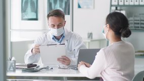 Male doctor in protective mask and lab coat sitting at desk in clinic, reading medical history of female patient and speaking with her during consultation. Covid-19 pandemic concept - Powered by Shutterstock - Get 15% off with code: PIKWIZARD15