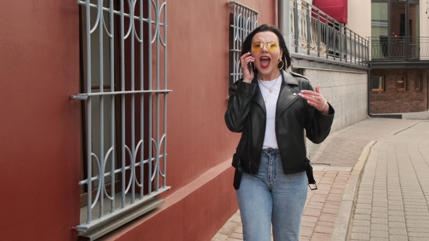 Angry and agressive woman screams and talks on the phone, curses and quarrels in rage. Yelling at the interlocutor talking and walking down the street. Woman call. Annoyed person talking mobile  Royalty-Free Stock Footage #1053542153