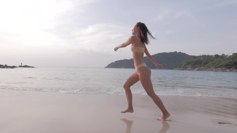 A beautiful sweet girl with a sexy body and excellent ass runs along the sandy beach overlooking palms and sea landscapes the ocean mountains and nature. Running girl on the beach in a swimsuit 