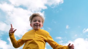 Happy child jumps very high on a trampoline against the blue sky. Blond boy jumps on a trampoline. Slow motion bottom view of a cheerful boy jumping on a trampoline. Children happiness.  - Powered by Shutterstock - Get 15% off with code: PIKWIZARD15