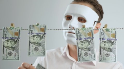 Masked anonymous laundering money. Dollars dry on clothespin rope. The concept of money laundering. Financial fraud. Financial crime. Legalization of criminal proceeds.