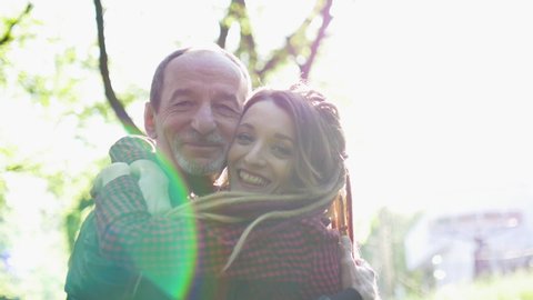 Senior father and adult daughter are embracing in the park during sunny day. Father's day concept
