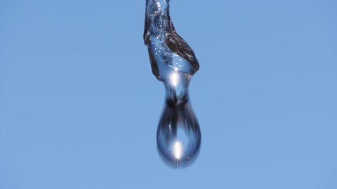 Incredible macro slow motion shot of water dripping from end of thawing icicle melting in spring with sunlight reflected inside. Looping possible.