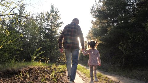 Rear View of Old Grandfather and Little Funny Talking Granddaughter Walking Along Summer Forest Path in Sunshine Holding Hands. Spend Leisure Time Together Outdoor for Carefree Lovely Family Happiness
