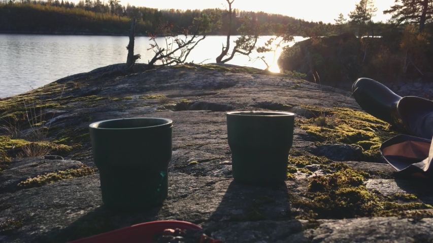 A traveler drinks tea from a mug and watches the sunset while sitting on Lake Ladoga Island